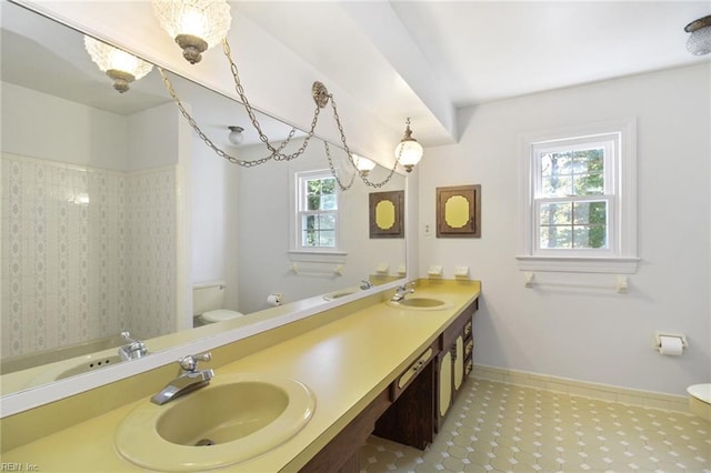 bathroom with baseboards, a sink, toilet, and double vanity