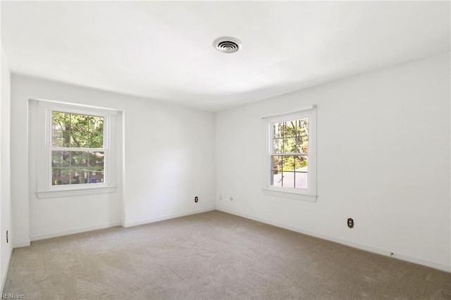 spare room featuring light colored carpet, visible vents, and baseboards