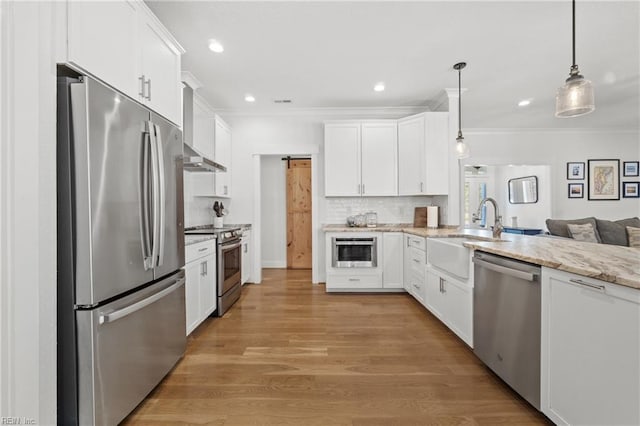 kitchen with appliances with stainless steel finishes, white cabinets, pendant lighting, and a barn door