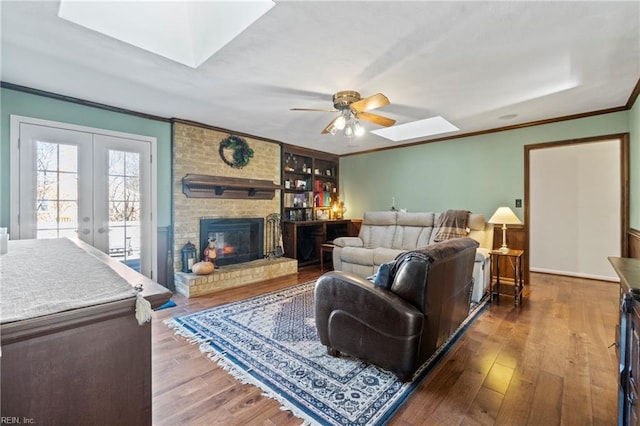 living room with a skylight, ceiling fan, crown molding, a fireplace, and dark hardwood / wood-style flooring