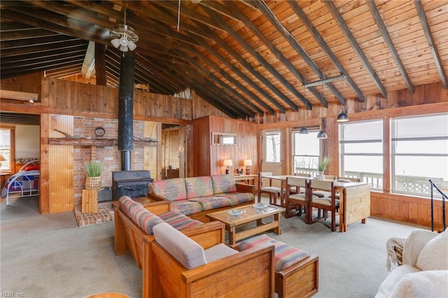 living room featuring vaulted ceiling with beams, light carpet, wood walls, and a wood stove