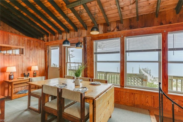 carpeted dining space with wooden ceiling, lofted ceiling with beams, and wooden walls