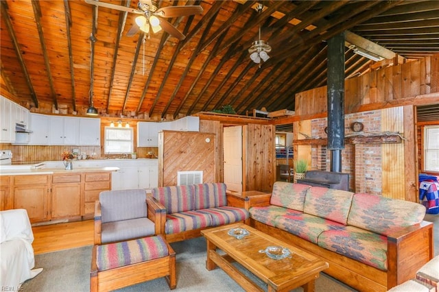 living room featuring a wood stove, wood walls, wooden ceiling, vaulted ceiling with beams, and ceiling fan