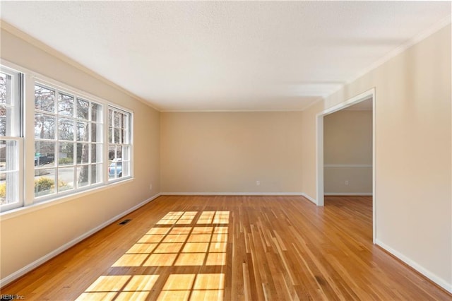 empty room with light wood finished floors, baseboards, visible vents, and crown molding