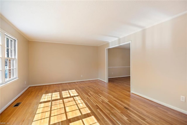 empty room featuring light wood finished floors, baseboards, visible vents, and ornamental molding