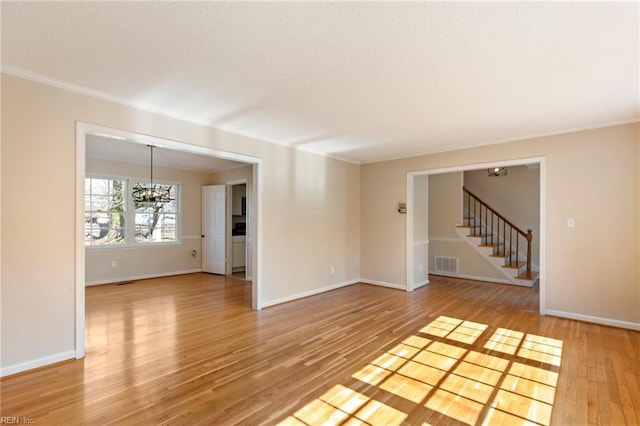 spare room featuring a notable chandelier, visible vents, light wood-style flooring, baseboards, and stairs