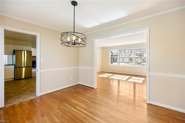 unfurnished dining area with light wood finished floors, a notable chandelier, baseboards, and crown molding