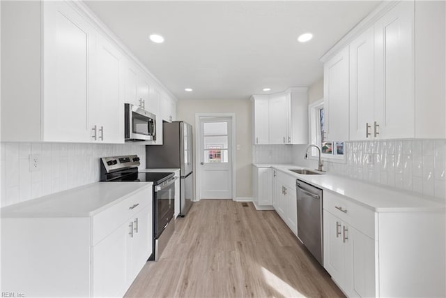 kitchen with sink, stainless steel appliances, white cabinetry, and light hardwood / wood-style floors