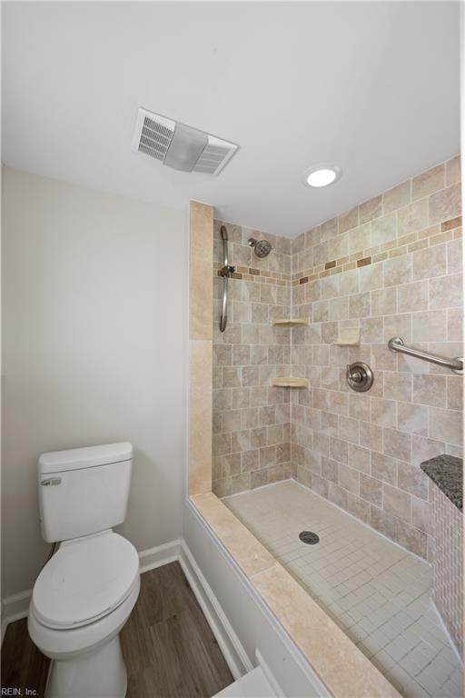 bathroom featuring hardwood / wood-style floors, a tile shower, and toilet