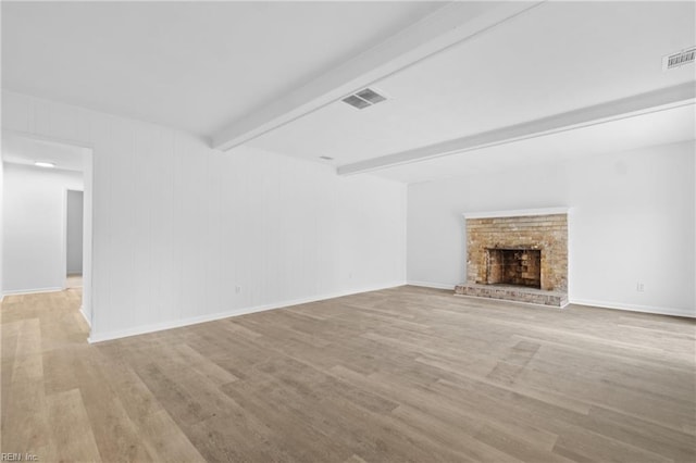 unfurnished living room featuring light wood-style flooring, a fireplace, visible vents, and beam ceiling