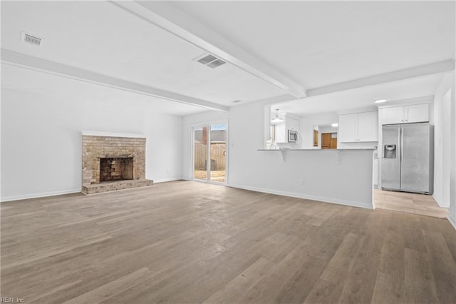 unfurnished living room with baseboards, light wood-style flooring, visible vents, and beamed ceiling