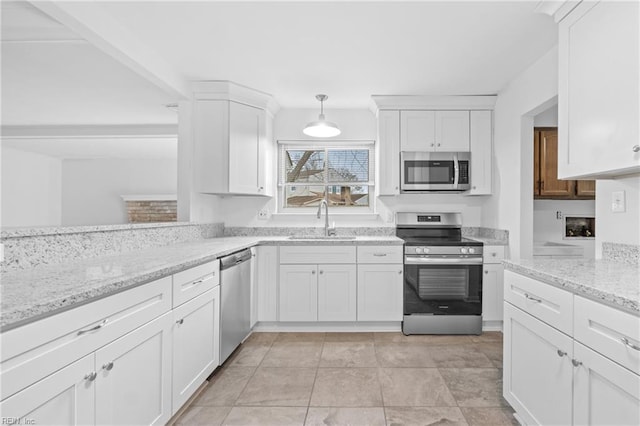 kitchen with hanging light fixtures, appliances with stainless steel finishes, white cabinets, a sink, and light stone countertops