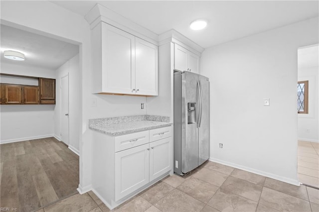 kitchen featuring baseboards, stainless steel fridge, light stone countertops, and white cabinets