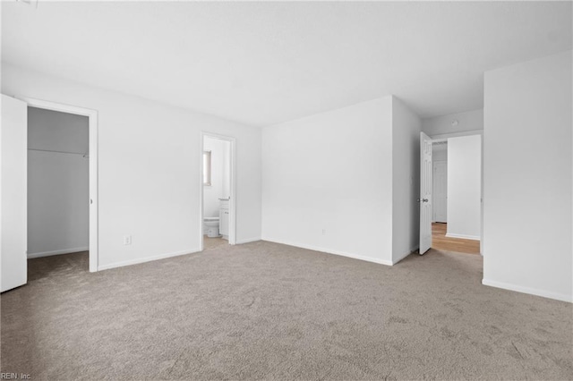 unfurnished bedroom with a spacious closet, baseboards, and light colored carpet