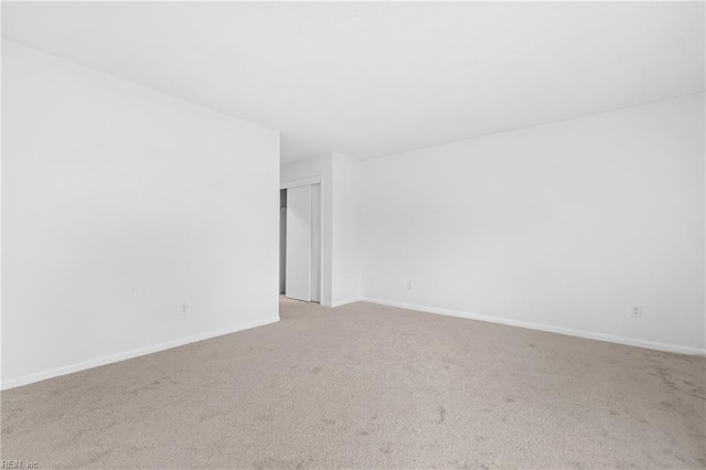 spare room featuring light carpet and baseboards