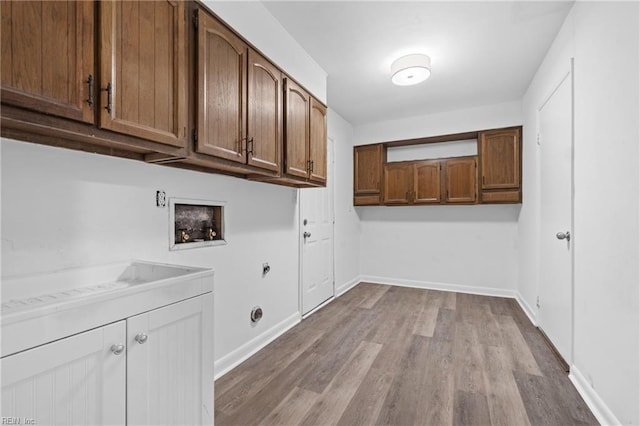 laundry area with gas dryer hookup, washer hookup, baseboards, light wood-style floors, and cabinet space