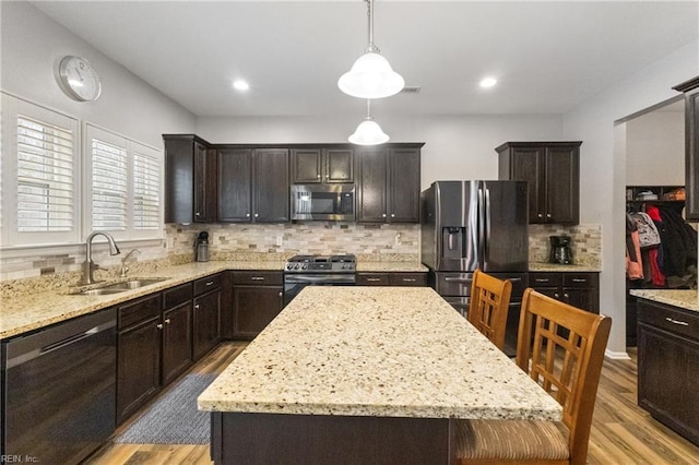 kitchen with appliances with stainless steel finishes, a center island, hanging light fixtures, dark brown cabinets, and a sink