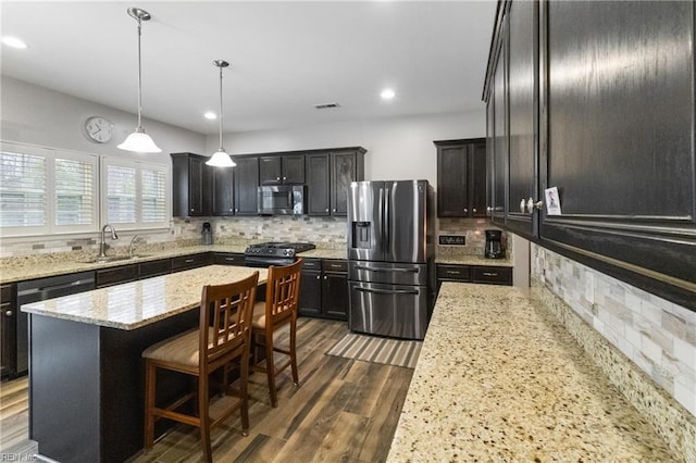 kitchen featuring a center island, decorative light fixtures, dark wood finished floors, appliances with stainless steel finishes, and a sink