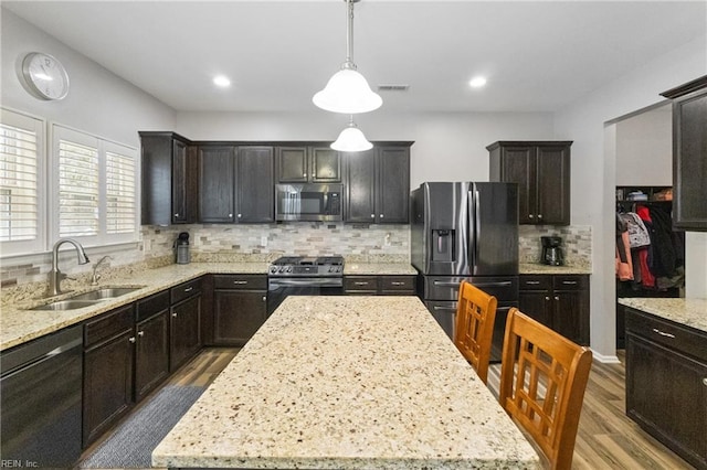 kitchen with hanging light fixtures, appliances with stainless steel finishes, a kitchen island, and a sink