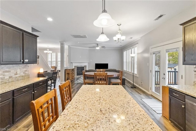 kitchen with decorative light fixtures, visible vents, a glass covered fireplace, dark brown cabinetry, and light stone countertops