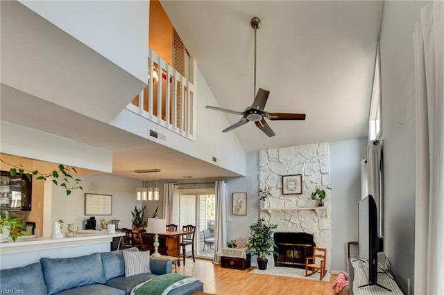 living room with visible vents, ceiling fan, a stone fireplace, wood finished floors, and high vaulted ceiling