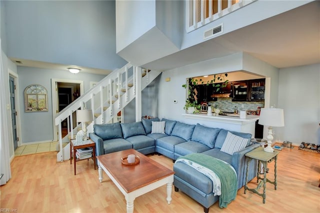 living area with stairs, light wood finished floors, a high ceiling, and visible vents