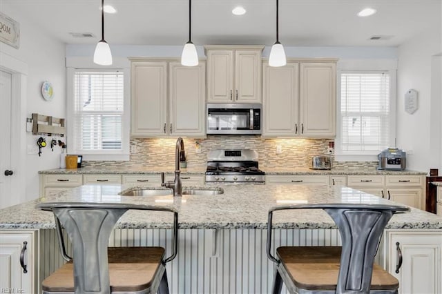 kitchen with a sink, stainless steel appliances, a center island with sink, and decorative light fixtures