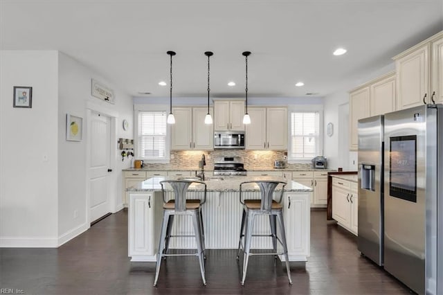 kitchen featuring pendant lighting, decorative backsplash, appliances with stainless steel finishes, a kitchen island, and light stone countertops