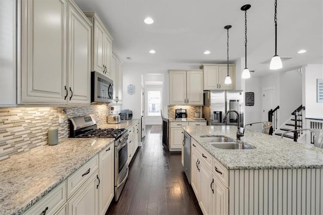 kitchen with stainless steel appliances, a sink, light stone countertops, and pendant lighting