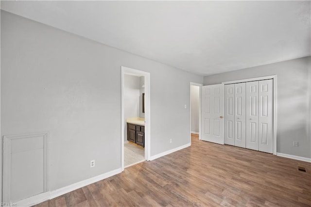 unfurnished bedroom featuring a closet, light hardwood / wood-style floors, and ensuite bath