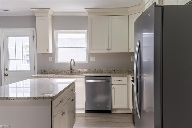 kitchen with light stone counters, appliances with stainless steel finishes, ornamental molding, white cabinets, and a sink