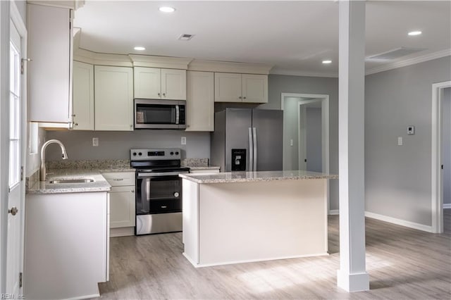 kitchen with a kitchen island, appliances with stainless steel finishes, ornamental molding, light stone countertops, and a sink