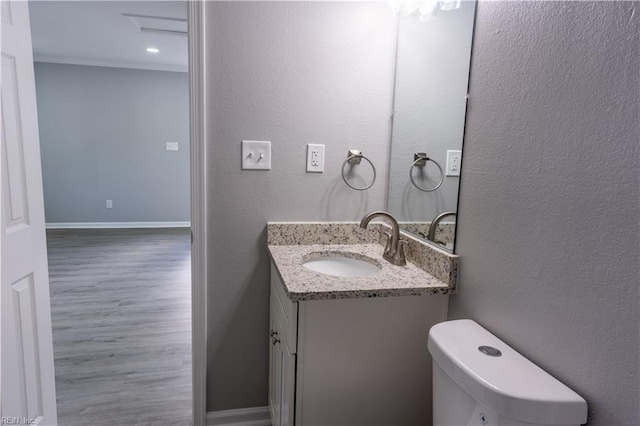 bathroom featuring a textured wall, toilet, vanity, wood finished floors, and baseboards