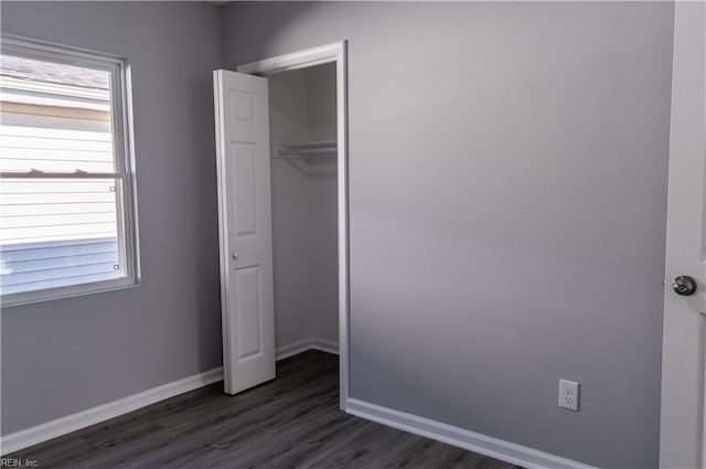 unfurnished bedroom featuring dark wood-style flooring, a closet, and baseboards