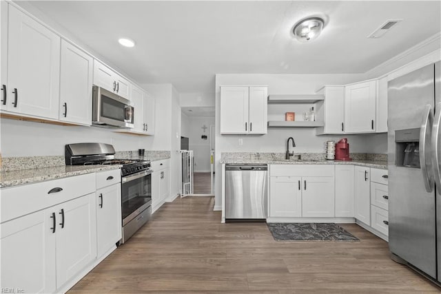 kitchen featuring stainless steel appliances, light stone countertops, hardwood / wood-style floors, sink, and white cabinetry
