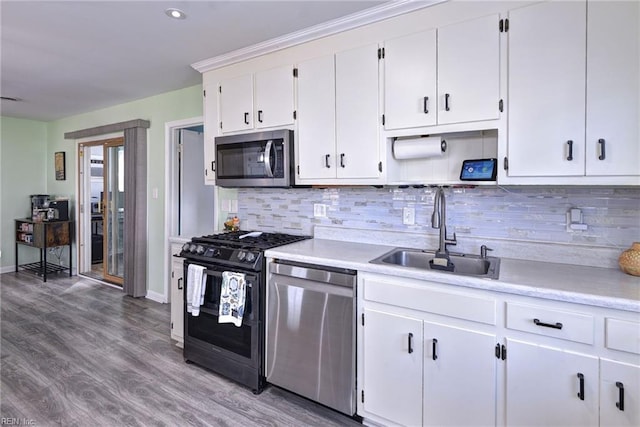 kitchen featuring white cabinets, appliances with stainless steel finishes, wood finished floors, light countertops, and a sink