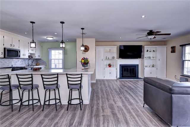 kitchen with white cabinetry, open floor plan, light countertops, hanging light fixtures, and stainless steel microwave