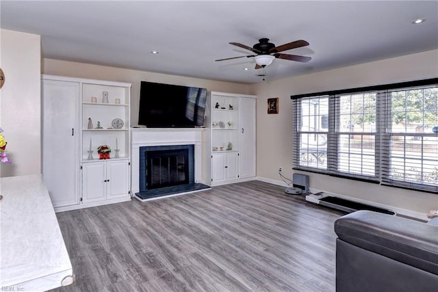 unfurnished living room with ceiling fan, wood finished floors, a glass covered fireplace, and a wealth of natural light