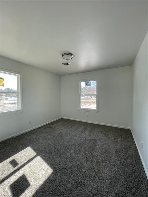 empty room with a wealth of natural light, visible vents, dark carpet, and baseboards