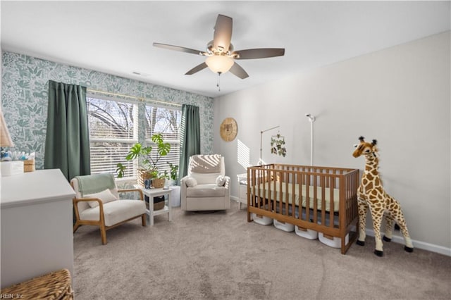 bedroom featuring a nursery area, carpet, baseboards, and ceiling fan