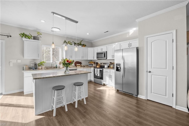 kitchen featuring light stone counters, hanging light fixtures, appliances with stainless steel finishes, white cabinets, and a kitchen island