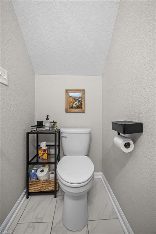 bathroom with vaulted ceiling, a textured wall, toilet, and baseboards