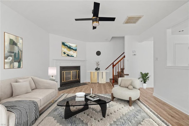 living room with a fireplace with flush hearth, baseboards, light wood-style flooring, visible vents, and stairway