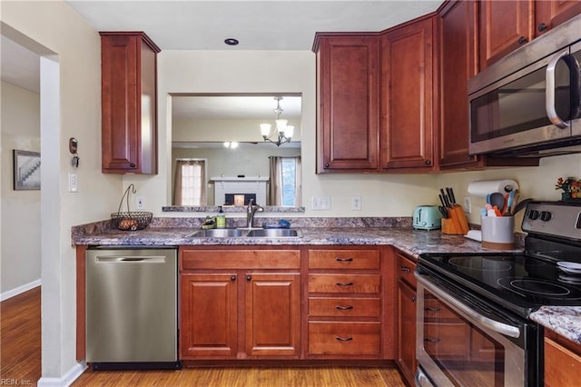 kitchen with dark stone counters, baseboards, appliances with stainless steel finishes, a sink, and light wood-style floors