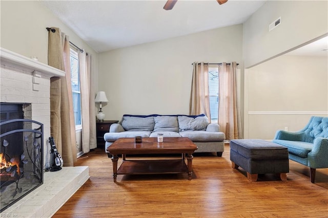 living area with visible vents, a brick fireplace, a ceiling fan, lofted ceiling, and wood finished floors