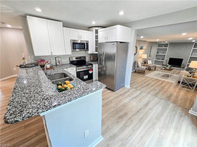 kitchen featuring a peninsula, a sink, white cabinetry, appliances with stainless steel finishes, and light wood finished floors