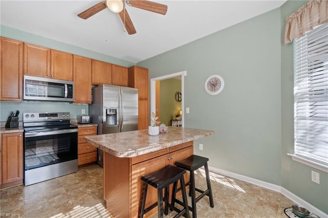 kitchen with a kitchen island, a breakfast bar area, brown cabinets, stainless steel appliances, and light countertops