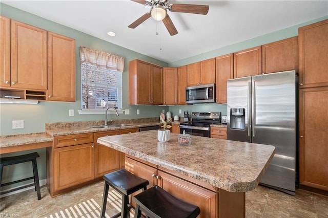 kitchen featuring ceiling fan, a kitchen island, a sink, a kitchen breakfast bar, and appliances with stainless steel finishes