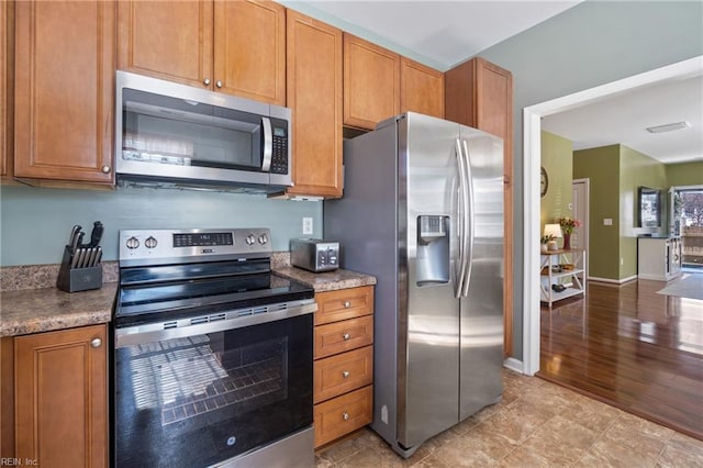 kitchen featuring brown cabinets, visible vents, baseboards, and stainless steel appliances