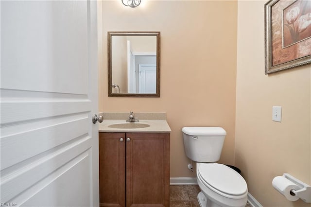 half bathroom featuring toilet, baseboards, and vanity